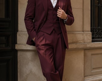 May include: A deep burgundy three-piece suit consisting of a tailored blazer, a matching button-up vest, and pleated trousers. The suit is worn over a crisp white collared shirt, paired with polished dark burgundy leather dress shoes.