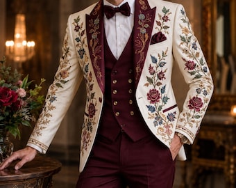 May include: A cream-colored blazer featuring intricate floral embroidery in shades of red, blue, and green, paired with a deep burgundy waistcoat, matching trousers, a white dress shirt, and a burgundy bow tie with a pocket square.