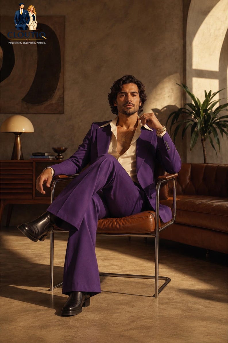 May include: A man in a purple suit, white shirt, and black boots sits in a brown leather chair. The suit jacket is open, revealing the shirt. The room has a retro vibe with a brown sofa and a lamp.