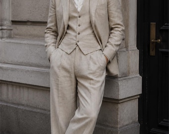 May include: A three-piece beige suit consisting of a single-breasted blazer, a button-up vest, and pleated trousers, worn with a white collared shirt and dark brown leather loafers. The suit features a textured fabric and a classic tailored fit.