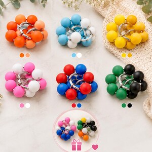 May include: A collection of circular keychains featuring clusters of smooth, matte-finish spherical beads in various colour combinations, including orange, blue, yellow, pink, red, and green, all attached to silver-toned metal rings.