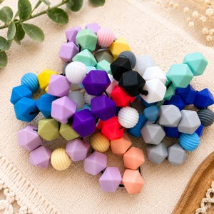 May include: A collection of multi-coloured silicone beads strung together on a black cord. The beads feature a mix of geometric hexagonal shapes and round ribbed textures in shades of purple, blue, yellow, pink, orange, black, white, and grey.