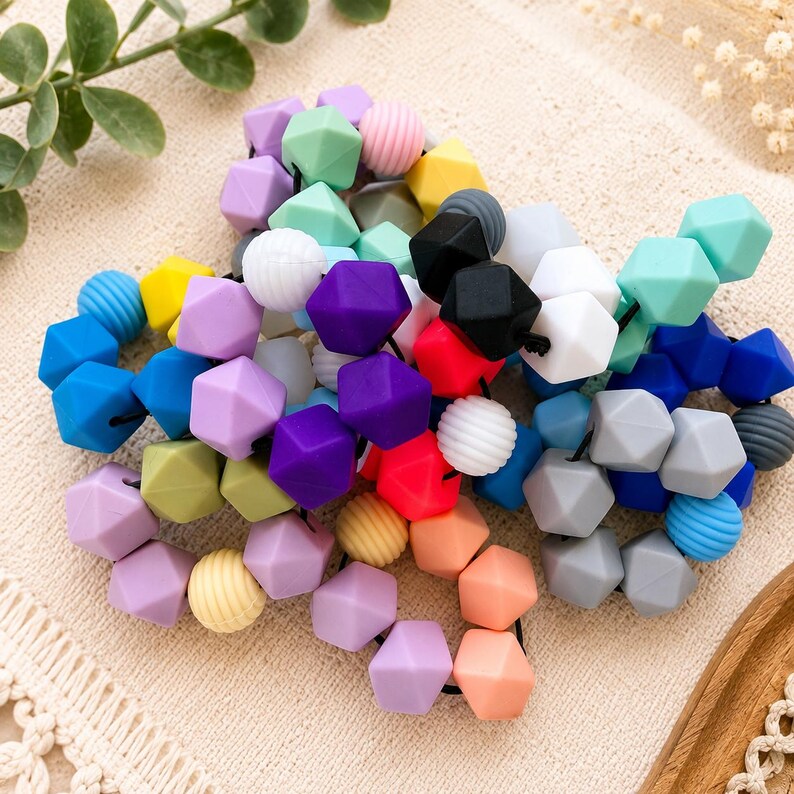 May include: A collection of multi-coloured silicone beads strung together on a black cord. The beads feature a mix of geometric hexagonal shapes and round ribbed textures in shades of purple, blue, yellow, pink, orange, black, white, and grey.
