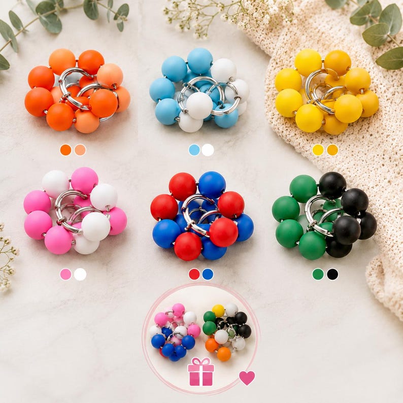 May include: A collection of circular keychains featuring clusters of smooth, matte-finish spherical beads in various colour combinations, including orange, blue, yellow, pink, red, and green, all attached to silver-toned metal rings.