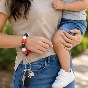 Peut inclure: Un porte-cl&eacute;s bracelet compos&eacute; d'un &eacute;lastique circulaire orn&eacute; de perles rondes alternant le noir, le blanc et le rouge, s&eacute;par&eacute;es par de petites entretoises argent&eacute;es. Un mousqueton argent&eacute; retient un anneau avec des cl&eacute;s et une breloque.