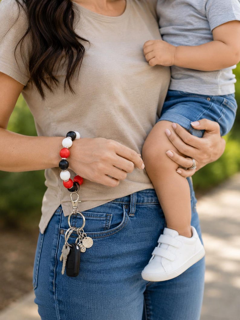 Peut inclure: Un porte-cl&eacute;s bracelet compos&eacute; d'un &eacute;lastique circulaire orn&eacute; de perles rondes alternant le noir, le blanc et le rouge, s&eacute;par&eacute;es par de petites entretoises argent&eacute;es. Un mousqueton argent&eacute; retient un anneau avec des cl&eacute;s et une breloque.