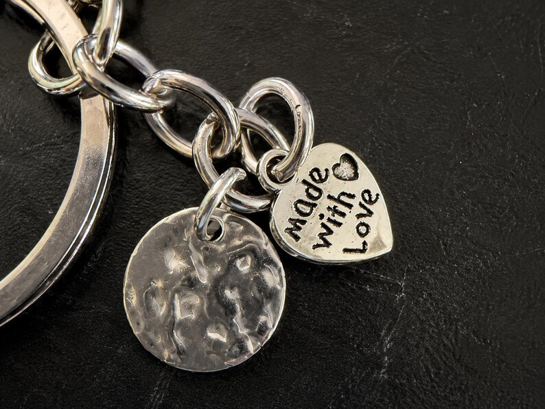 Peut inclure: Un porte-cl&eacute;s en m&eacute;tal argent&eacute; compos&eacute; d'un anneau circulaire, d'une breloque ronde textur&eacute;e et d'une breloque en forme de c&oelig;ur. Le c&oelig;ur est grav&eacute; avec le texte "made with love" et comporte un petit symbole de c&oelig;ur au-dessus du mot "with".