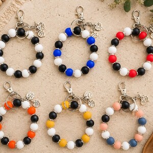 Peut inclure: Six porte-cl&eacute;s circulaires en perles de silicone avec des fermoirs mousquetons en m&eacute;tal et de petites breloques rondes. Les perles sont dispos&eacute;es en divers motifs de couleurs, notamment noir et blanc, bleu et blanc, rouge et blanc, orange et noir, jaune et noir, ainsi que des combinaisons de bleu pastel, rose et blanc.