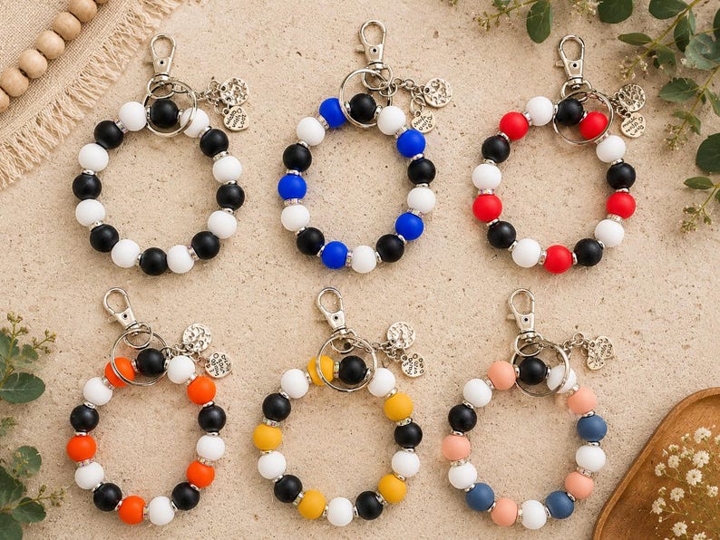 Peut inclure: Six porte-cl&eacute;s circulaires en perles de silicone avec des fermoirs mousquetons en m&eacute;tal et de petites breloques rondes. Les perles sont dispos&eacute;es en divers motifs de couleurs, notamment noir et blanc, bleu et blanc, rouge et blanc, orange et noir, jaune et noir, ainsi que des combinaisons de bleu pastel, rose et blanc.
