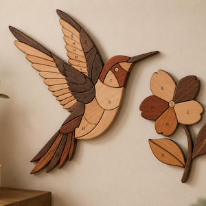 Könnte beinhalten: Wandkunst aus Holz mit einem Kolibri und einer Blume. Der Kolibri ist im Flug mit ausgebreiteten Flügeln, und die Blume hat fünf Blütenblätter. Die Kunstwerke bestehen aus verschiedenen Brauntönen und sind an einer hellen Wand befestigt.