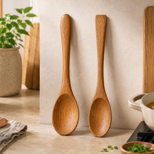 May include: Two wooden spoons with smooth, rounded bowls and long, tapered handles. One spoon features a rounded handle end, while the other has a flat, squared-off handle end. Both spoons exhibit a natural light brown wood grain texture.