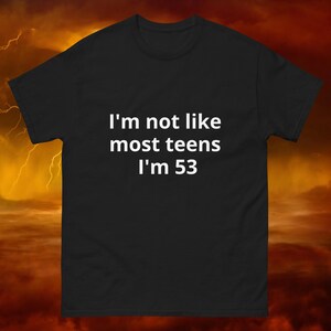 Puede incluir: Camiseta negra con el texto blanco "I'm not like most teens I'm 53". La camiseta es de manga corta y cuello redondo. El fondo es un degradado naranja oscuro y amarillo con rayos.