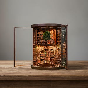 May include: A detailed, illuminated wooden bookshelf diorama with an open door. The interior features miniature books, a spiral staircase, and a small tree. The warm lighting highlights the intricate details of the handcrafted piece.