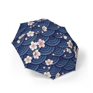 May include: A navy blue umbrella with a repeating wave pattern and branches of white and pink cherry blossoms. The umbrella is open, showcasing the floral design.