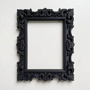 May include: A black rectangular picture frame with elaborate, swirling patterns. The frame has a matte finish and a traditional, vintage appearance. The frame is empty, with a white background visible through the opening. Suitable for displaying photos or artwork.