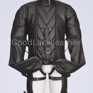 May include: A black leather restraint suit featuring a quilted torso, long sleeves with integrated hand enclosures, and a high collar with a metal ring. The garment includes adjustable buckled straps across the chest and legs, with the text GoodLuckLeather.