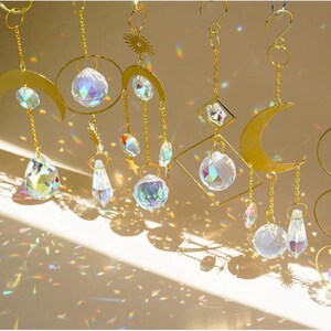 May include: A collection of gold-toned metal suncatchers featuring various geometric shapes including crescents, circles, and diamonds. Each piece is adorned with clear, multifaceted glass crystals that refract light into colorful rainbows.