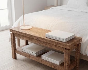 May include: A rectangular wooden bench with a natural brown finish and a lower storage shelf. The bench features a thick, textured top surface and four sturdy legs. Several stacks of plain white books are placed on the top and bottom shelves.