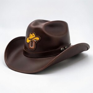 Gorro vaquero marrón estilo western con parche de la letra U amarilla y detalles metálicos.