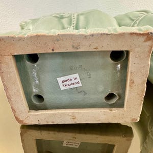 May include: A light green ceramic base with a crackle glaze finish, featuring a rectangular shape with four circular openings on the underside. A white sticker with the text Made in Thailand is affixed to the center of the base surface.