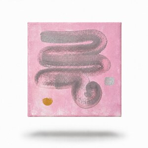 以下が含まれることがあります： 淡いピンクの背景に、渦巻き状にカーブした大きな質感のあるダークグレーの水平な筆跡が描かれた正方形のキャンバス画。左下に小さな金の円、右側に小さな銀の正方形が配置されています。