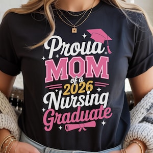 May include: Black t-shirt with the text "Proud Mom of a 2026 Nursing Graduate" in white and pink. The design includes a graduation cap and a diploma. The shirt is a crew neck.