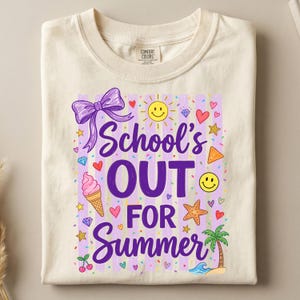 以下が含まれることがあります： 「School's Out For Summer」と紫色のグラフィックがプリントされた、クリーム色のTシャツ。デザインには、リボン、ハート、笑顔の太陽、アイスクリーム、ヒトデ、ヤシの木が含まれています。Tシャツは折りたたまれています。