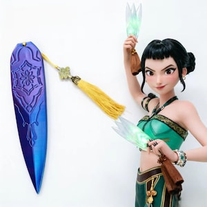 Puede incluir: Figura de una mujer con un atuendo verde y dorado, sosteniendo dos abanicos brillantes. A la izquierda cuelga una larga pieza decorativa morada y azul con una borla dorada. La mujer tiene el pelo negro y sonríe.