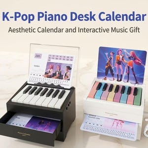 Puede incluir: Dos calendarios de escritorio con forma de piano. Uno es negro con un teclado blanco, el otro es blanco con un teclado colorido. Ambos tienen un cajón y una pantalla de calendario con imágenes de grupos de K-Pop. El texto de la imagen dice "K-Pop Piano Desk Calendar".