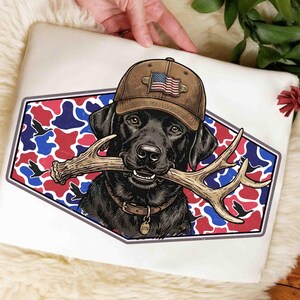Può includere: Una custodia bianca per laptop con un Labrador Retriever nero che indossa un berretto marrone con una bandiera americana. Il cane tiene un corno in bocca, su uno sfondo mimetico rosso, bianco e blu.