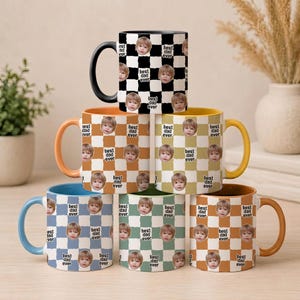May include: A stack of six ceramic mugs featuring a checkered pattern in various colors. Each mug displays repeating circular portraits of a child and the text "best dad ever" printed within the squares. Each mug has a solid colored handle.