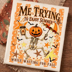 Può includere: Una t-shirt bianca con la grafica di uno scheletro con testa di zucca che tiene in mano una tazza di caffè e un ombrello. Il testo recita "ME TRYING TO ENJOY SUMMER WHILE WAITING FOR FALL" circondato da stelle arancioni e gialle e pipistrelli neri.