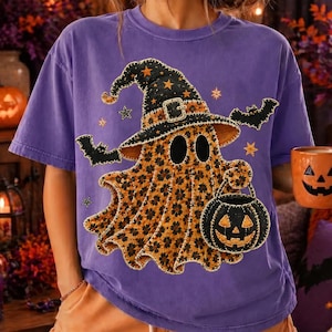 May include: A purple short-sleeve t-shirt featuring a central graphic of a ghost wearing a witch hat and holding a jack-o'-lantern bucket. The ghost has a leopard print pattern, and the design includes black bats and orange stars surrounding it.