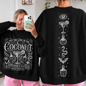 May include: A black long-sleeve sweatshirt featuring a white graphic print. The front displays a margarita glass, potion bottles, a snake, and the text "PUT THE LIME IN THE COCONUT AND DRINK IT ALL UP MIDNIGHT MARGARITAS." The back shows a vertical design.