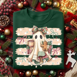 May include: A dark green crewneck sweatshirt featuring a graphic of a ghost wearing a floral bow, holding a mug and a gingerbread man. The ghost is layered over horizontal beige brushstrokes with red and green plaid accents and string lights.