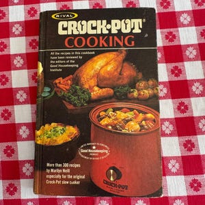 May include: Vintage "Crock-Pot Cooking" cookbook by Marilyn Neill. The cover features a roasted turkey, vegetables, and a slow cooker filled with stew. The cookbook is on a red and white checkered tablecloth.