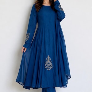 May include: A deep blue long-sleeved dress with a flared skirt and matching trousers. The dress features gold-toned embroidery on the cuffs and a central floral motif on the lower front. The fabric has a sheer, layered appearance with a round neckline.