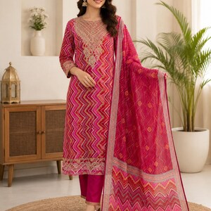 Puede incluir: Un conjunto de tres piezas en fucsia y rosa que consta de una túnica de manga larga con patrón de chevrón y bordados dorados en el cuello y el dobladillo, pantalones fucsia lisos y una dupatta transparente a juego con un borde decorativo.