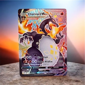 May include: A Charizard VMAX trading card featuring a black and white dragon-like creature with orange flames, 330 HP, and the attacks Claw Slash and G-Max Wildfire. The card has a holographic finish with silver accents and text details.