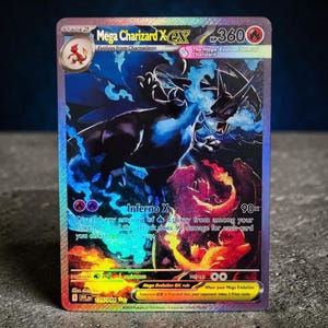 May include: A holographic Mega Charizard X EX trading card with 360 HP. The card features a dark dragon-like creature surrounded by blue flames, with smaller illustrations of Charizard and Charmander below. Text includes Inferno X and 90x.