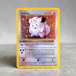 May include: A holographic Clefairy trading card with a yellow border. The card displays the character Clefairy, 40 HP, and the attacks Sing and Metronome. It includes text detailing the Fairy Pokémon, length of 2' 0", weight of 17 lbs, and 1999 copyright information.