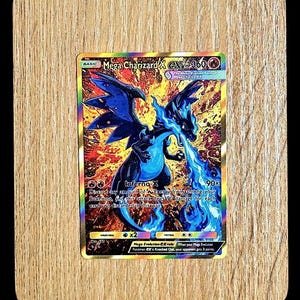 May include: A holographic Mega Charizard X trading card featuring a black and blue dragon-like creature breathing blue flames against a fiery orange and yellow background. The card displays the text Mega Charizard X, 360 HP, and Inferno X.