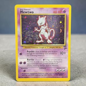 May include: A holographic Mewtwo trading card with a yellow border and purple background. The card displays the character illustration, 60 HP, Psychic and Barrier attacks, and text including Genetic Pokémon, Length: 6' 7", Weight: 269 lbs, and 10/130.