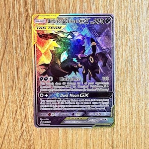 May include: A holographic Umbreon and Darkrai Tag Team trading card with 270 HP. The card features a dark, iridescent design with purple and black tones, displaying the Black Lance and Dark Moon GX attacks, along with game rules and symbols.