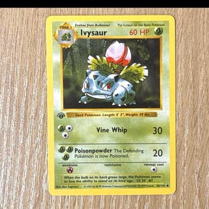 May include: A Pokémon trading card featuring Ivysaur, a Stage 1 Seed Pokémon. The card has a green and white design with the text "Ivysaur" and "60 HP." It includes the "Vine Whip" and "Poisonpowder" attacks. The card's length is 3' 3" and weighs 29 lbs.
