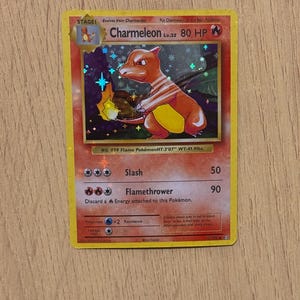 Puede incluir: Una carta coleccionable de Pokémon Charmeleon. La carta presenta una ilustración de Charmeleon naranja con el texto "Charmeleon Lv.32 80 HP". La carta tiene un fondo holográfico e incluye detalles de ataque.