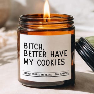 May include: A lit soy candle in a brown glass jar with a white label. The label reads "Bitch, Better Have My Cookies." The candle is hand-poured in Texas. The lid is black.