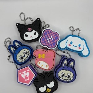 May include: A collection of colorful character keychains. The keychains feature various designs, including a black cat, a pink bunny, and a blue dog. Each keychain is attached to a silver chain.