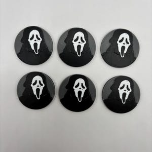 May include: Six black round buttons with a white Ghostface mask design. The buttons are glossy and have a simple, yet recognizable, horror movie theme. The buttons are arranged in two rows of three.