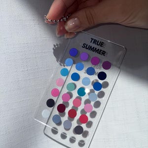 May include: A silver beaded ring is held above a clear plastic color palette. The palette features a grid of colorful dots in shades of blue, pink, purple, and more. The text "TRUE SUMMER" is printed on the palette.